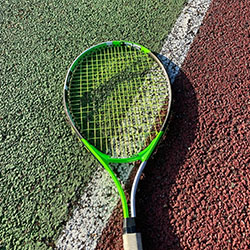 Green tennis racket laying on a tennis court